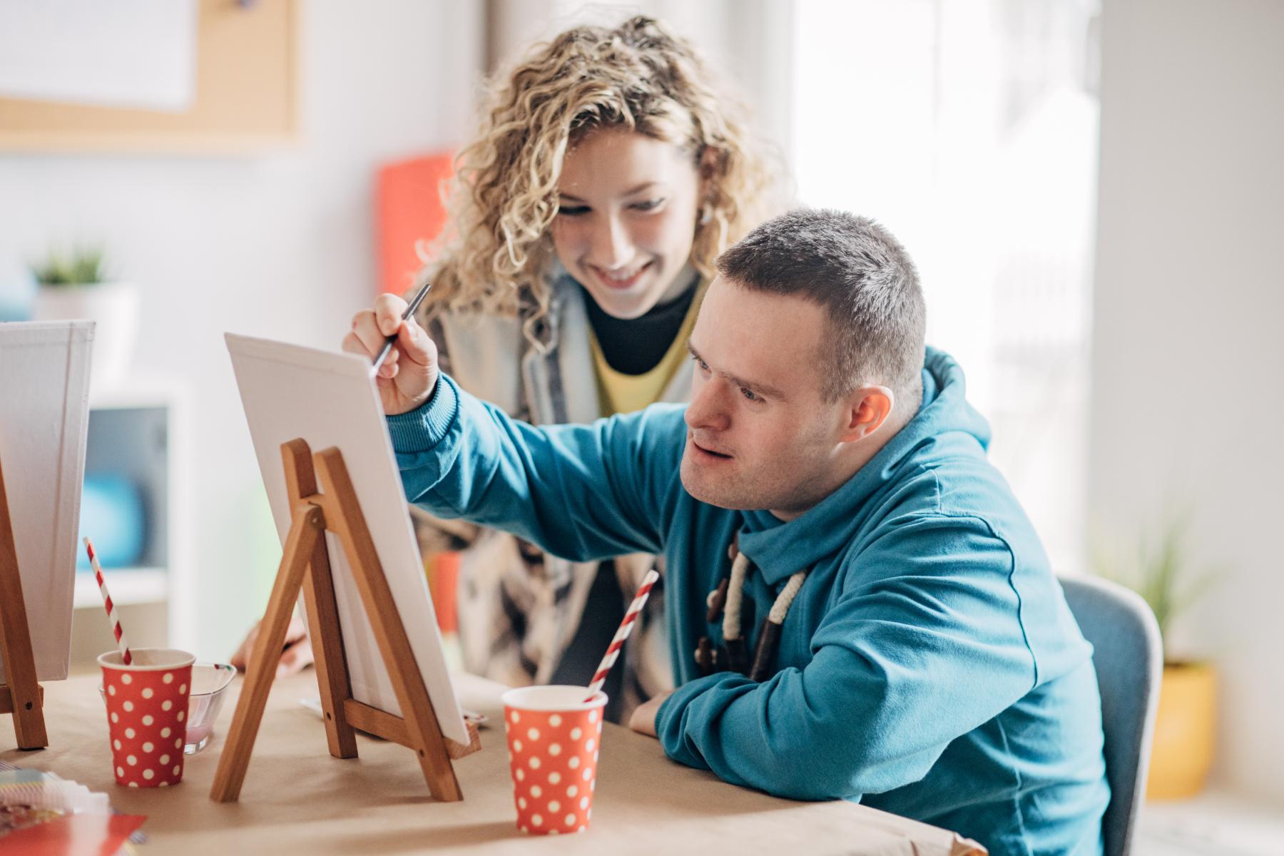 direct support professional helping developmentally disabled man paint on a canvas